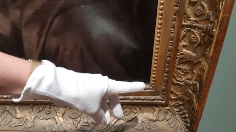 Hand mit Handschuh zeigt auf einen Bilderrahmen